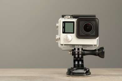 Photo of Modern action camera and mount on table against grey background. Space for text