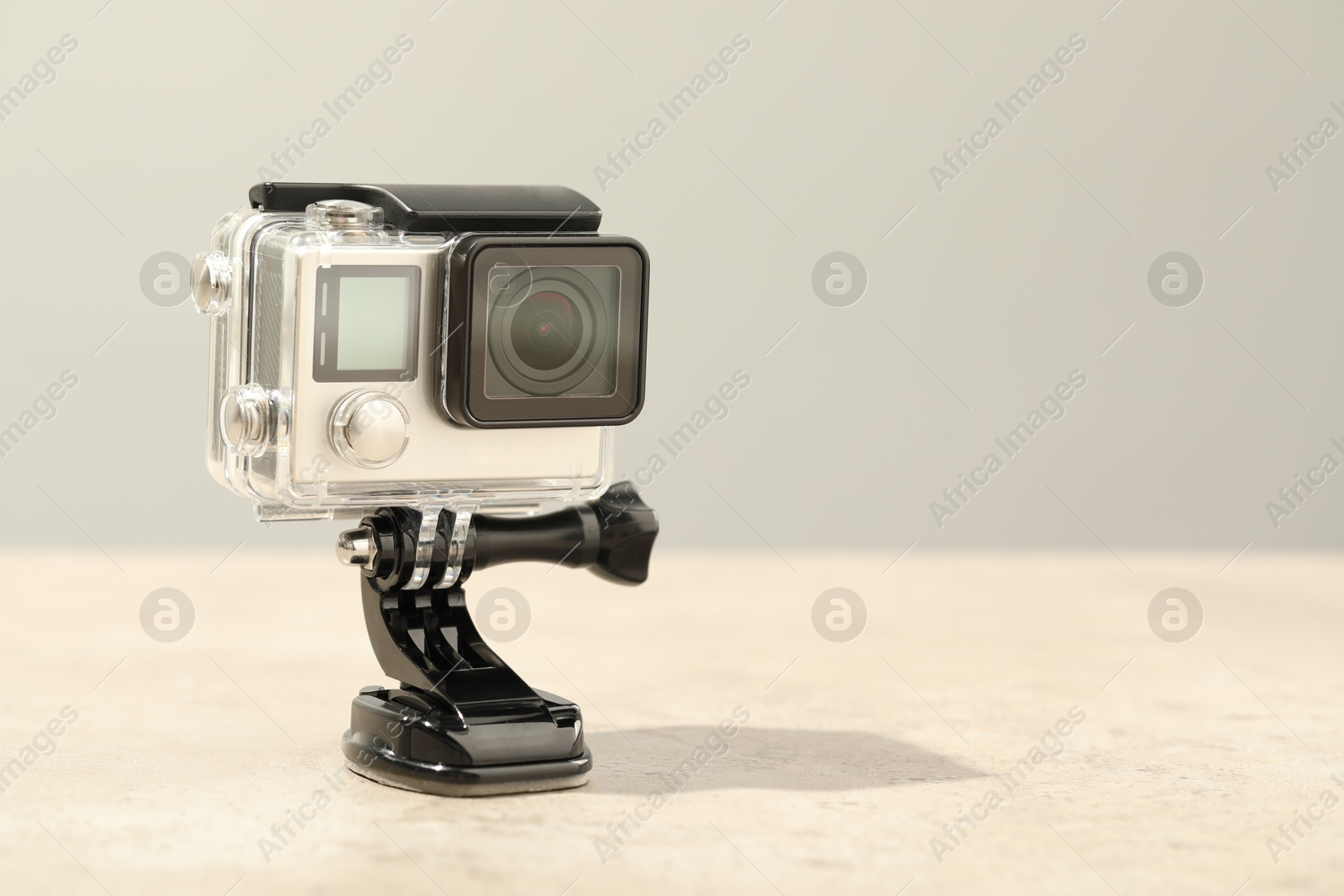 Photo of Modern action camera and mount on table against grey background. Space for text