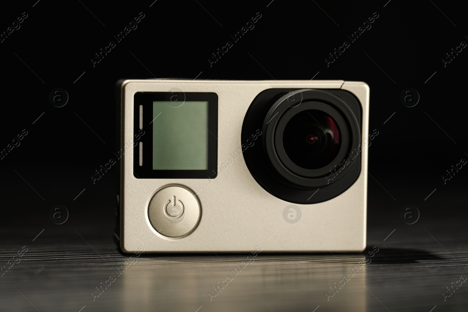 Photo of Modern action camera on wooden table against black background, closeup