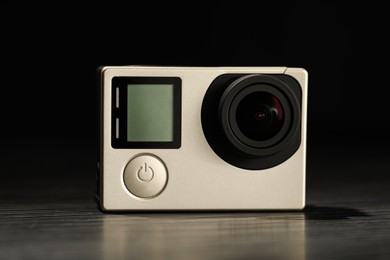 Modern action camera on wooden table against black background, closeup