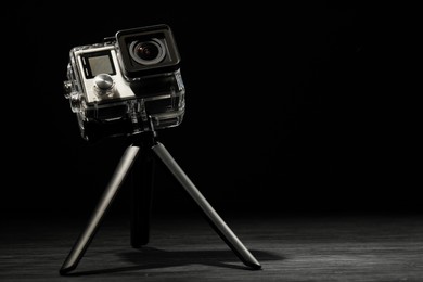 Photo of Modern action camera and tripod on wooden surface against black background. Space for text