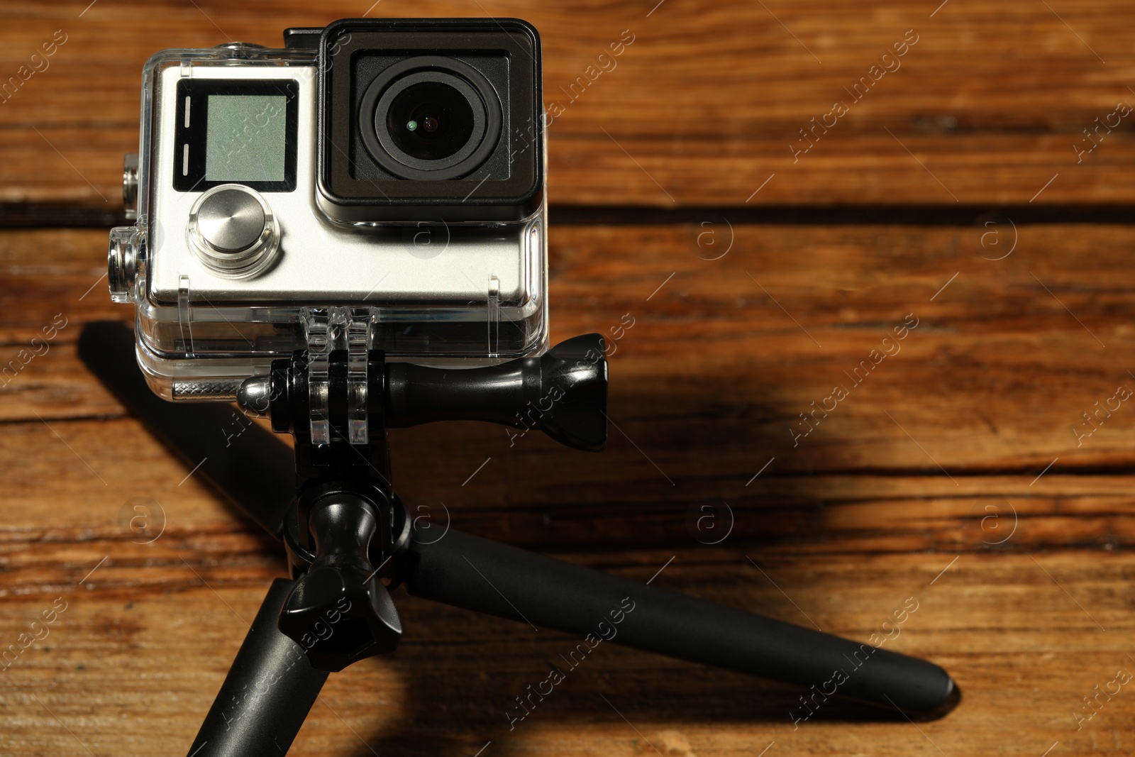 Photo of Modern action camera and tripod on wooden surface, closeup. Space for text