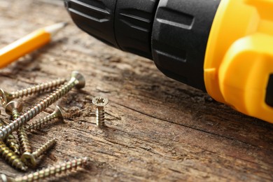 Photo of Electric screwdriver and screws on wooden plank, closeup