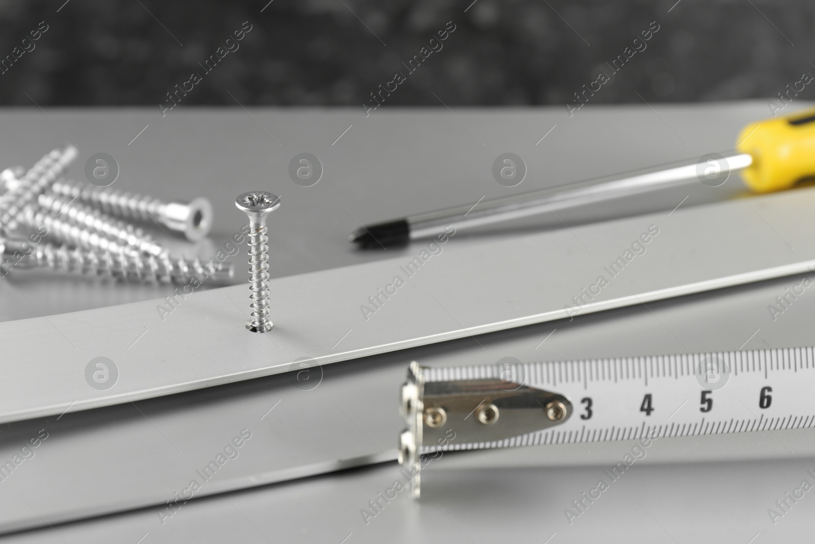 Photo of Metal screw in white panel and tools on light table, closeup