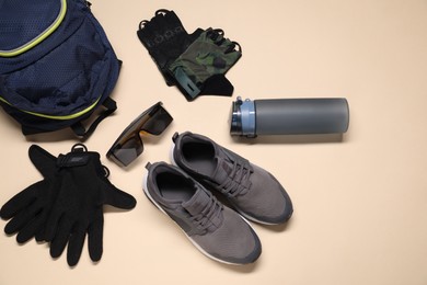 Backpack, sneakers, cycling gloves, bottle and goggles on pale yellow background, flat lay