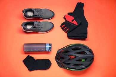 Photo of Bicycle helmet, sportswear, sneakers and thermo bottle on coral background, flat lay