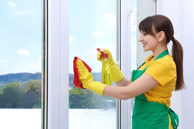 Housewife with spray bottle of detergent and napkin cleaning window indoors