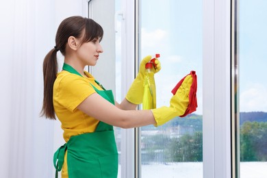 Housewife with spray bottle of detergent and napkin cleaning window indoors