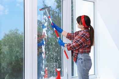 Beautiful young woman with squeegee tool cleaning window indoors