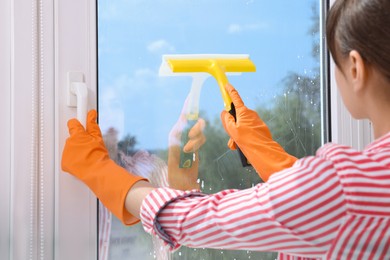 Housewife with squeegee cleaning window indoors, back view