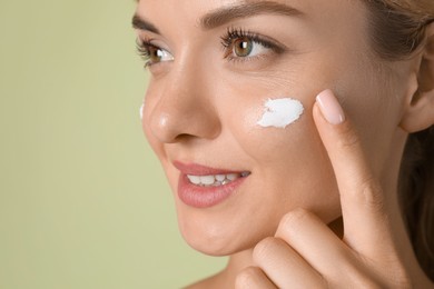 Photo of Beautiful woman applying cream on her face against green background, closeup