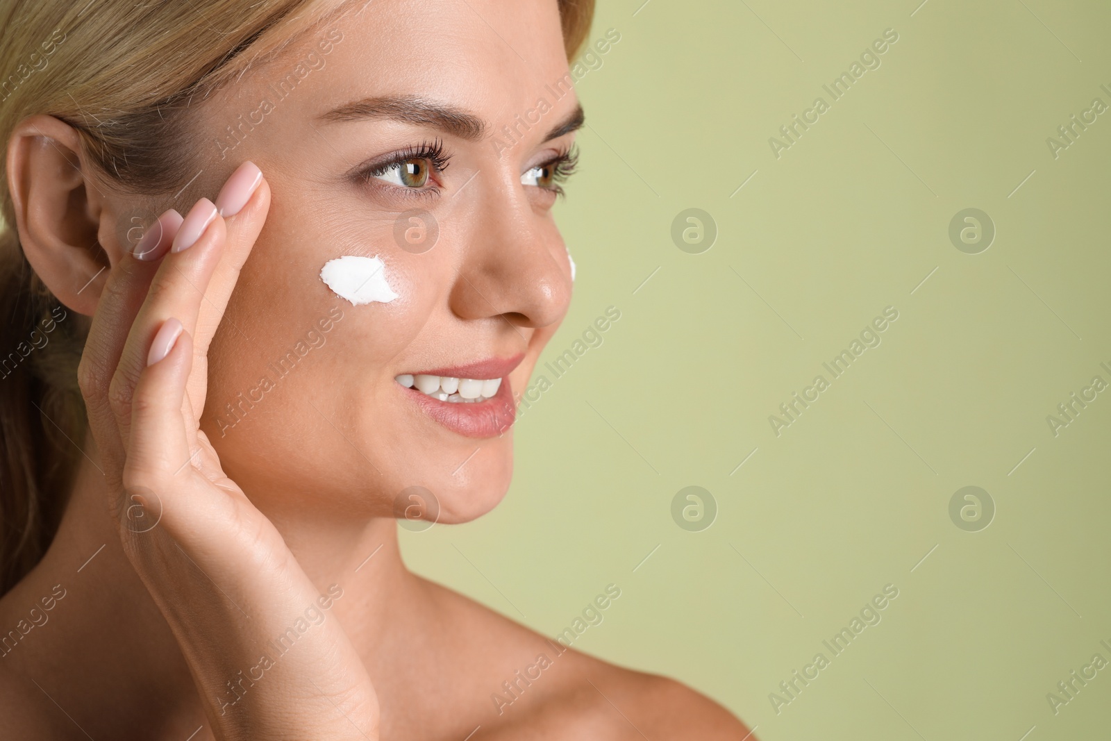 Photo of Beautiful woman with cream on her face against green background, closeup. Space for text