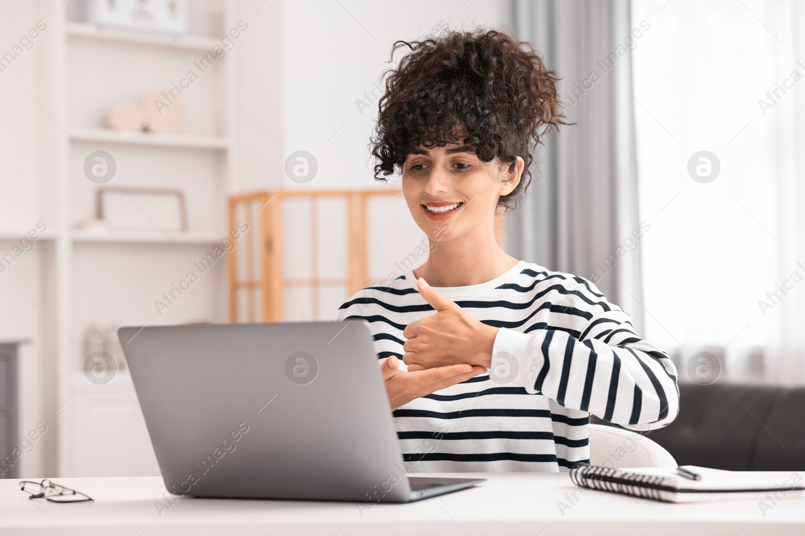 Photo of Young woman using sign language for communication during video call at white table indoors