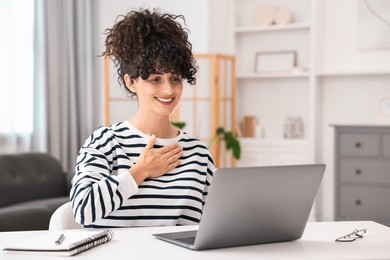 Photo of Young woman using sign language for communication during video call at white table indoors