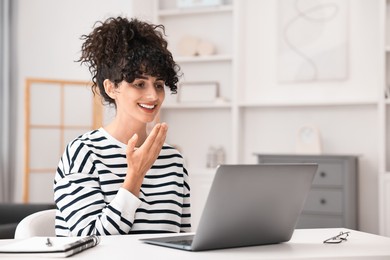 Young woman using sign language for communication during video call at white table indoors