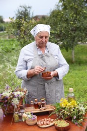 Senior woman with different ingredients for tincture at table outdoors