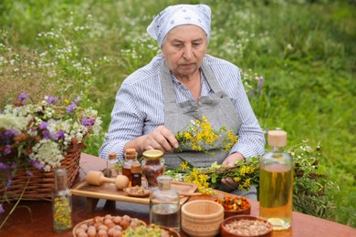 Senior woman with different ingredients for tincture at wooden table outdoors