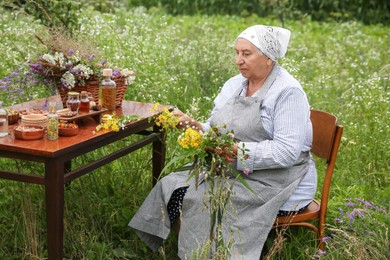 Senior woman with different ingredients for tincture at wooden table outdoors