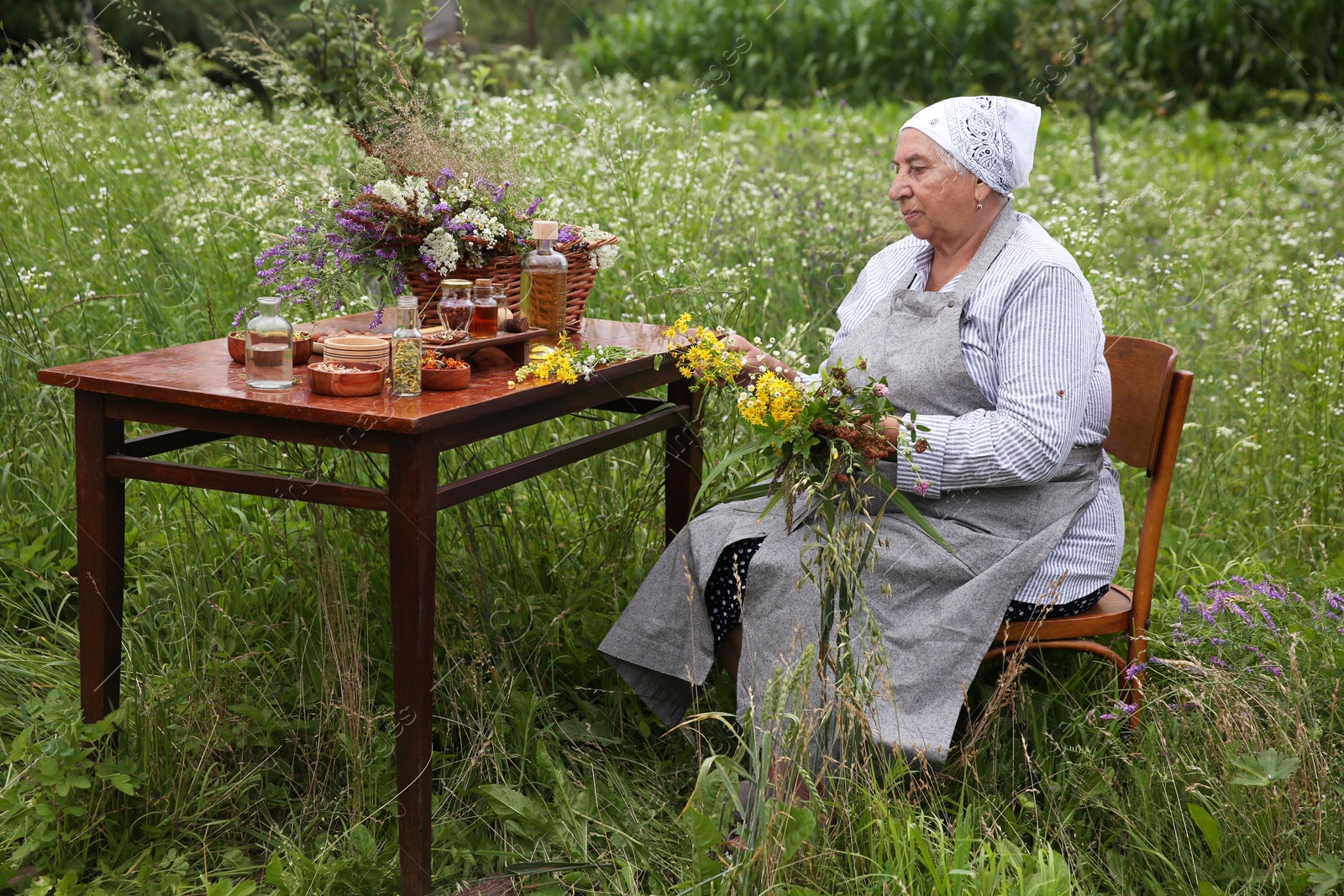 Photo of Senior woman with different ingredients for tincture at wooden table outdoors