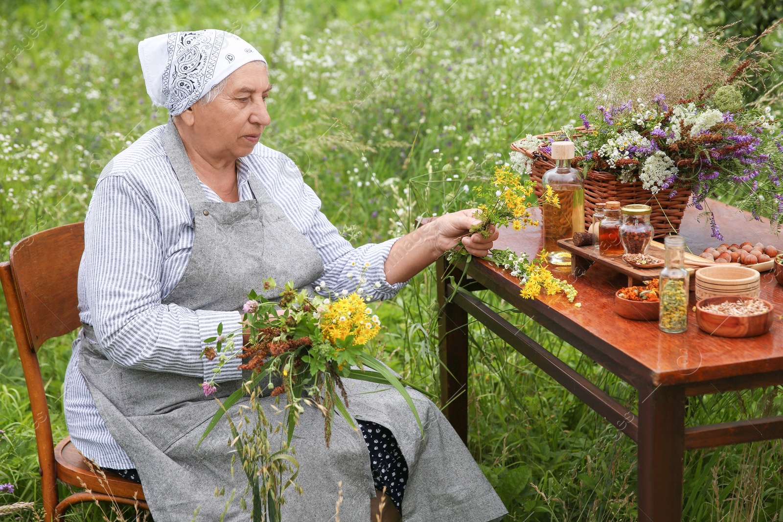 Photo of Senior woman with different ingredients for tincture at wooden table outdoors