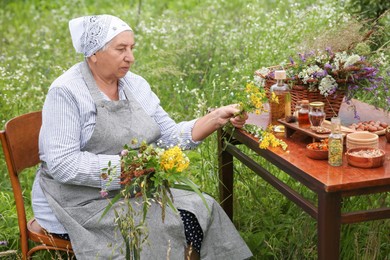 Senior woman with different ingredients for tincture at wooden table outdoors