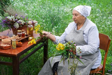 Photo of Senior woman with different ingredients for tincture at wooden table outdoors