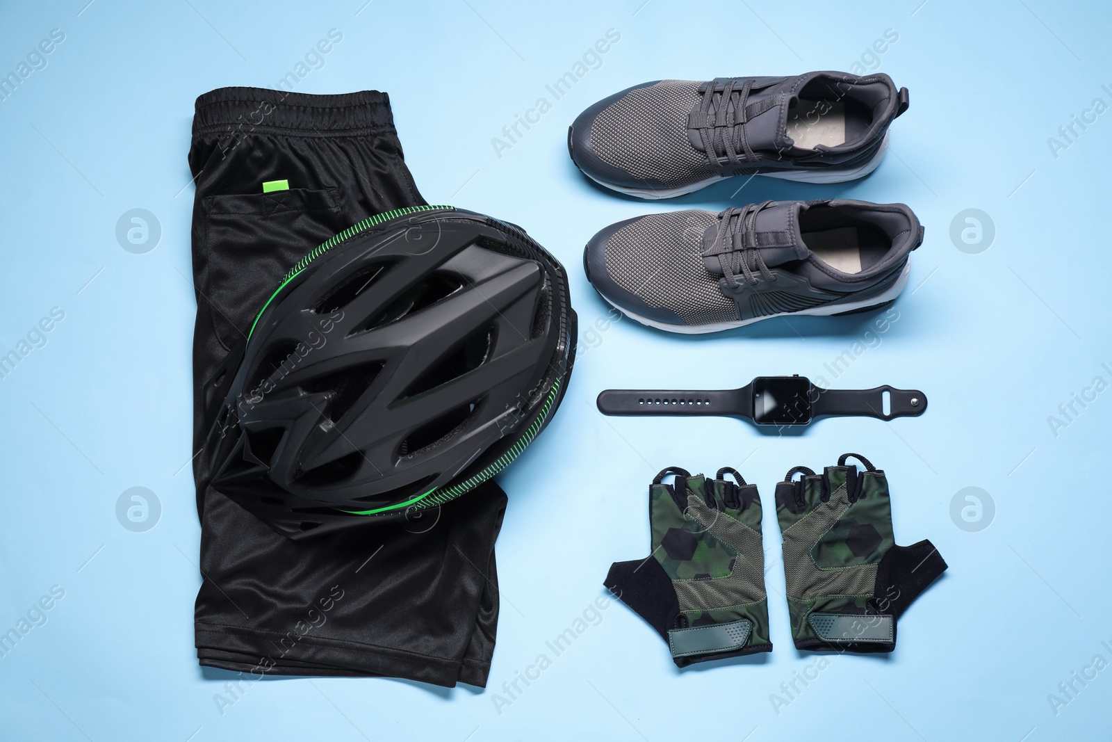 Photo of Bicycle helmet, sneakers, sportswear and wristwatch on light blue background, flat lay