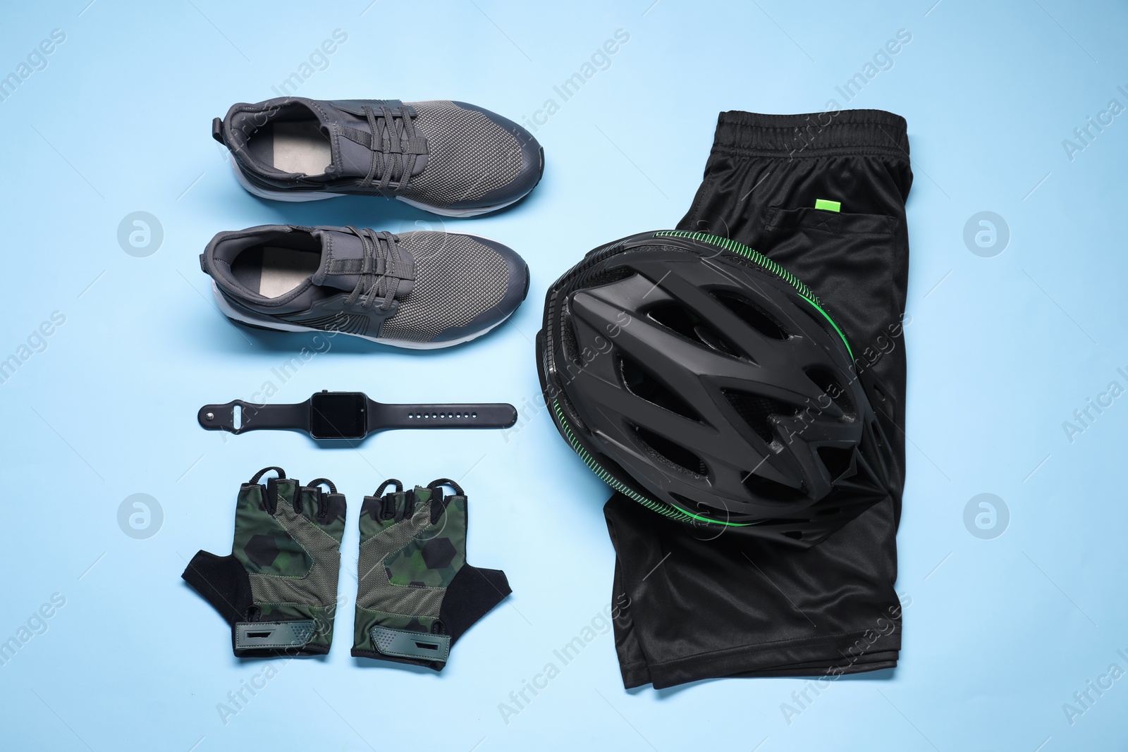 Photo of Bicycle helmet, sneakers, sportswear and wristwatch on light blue background, flat lay