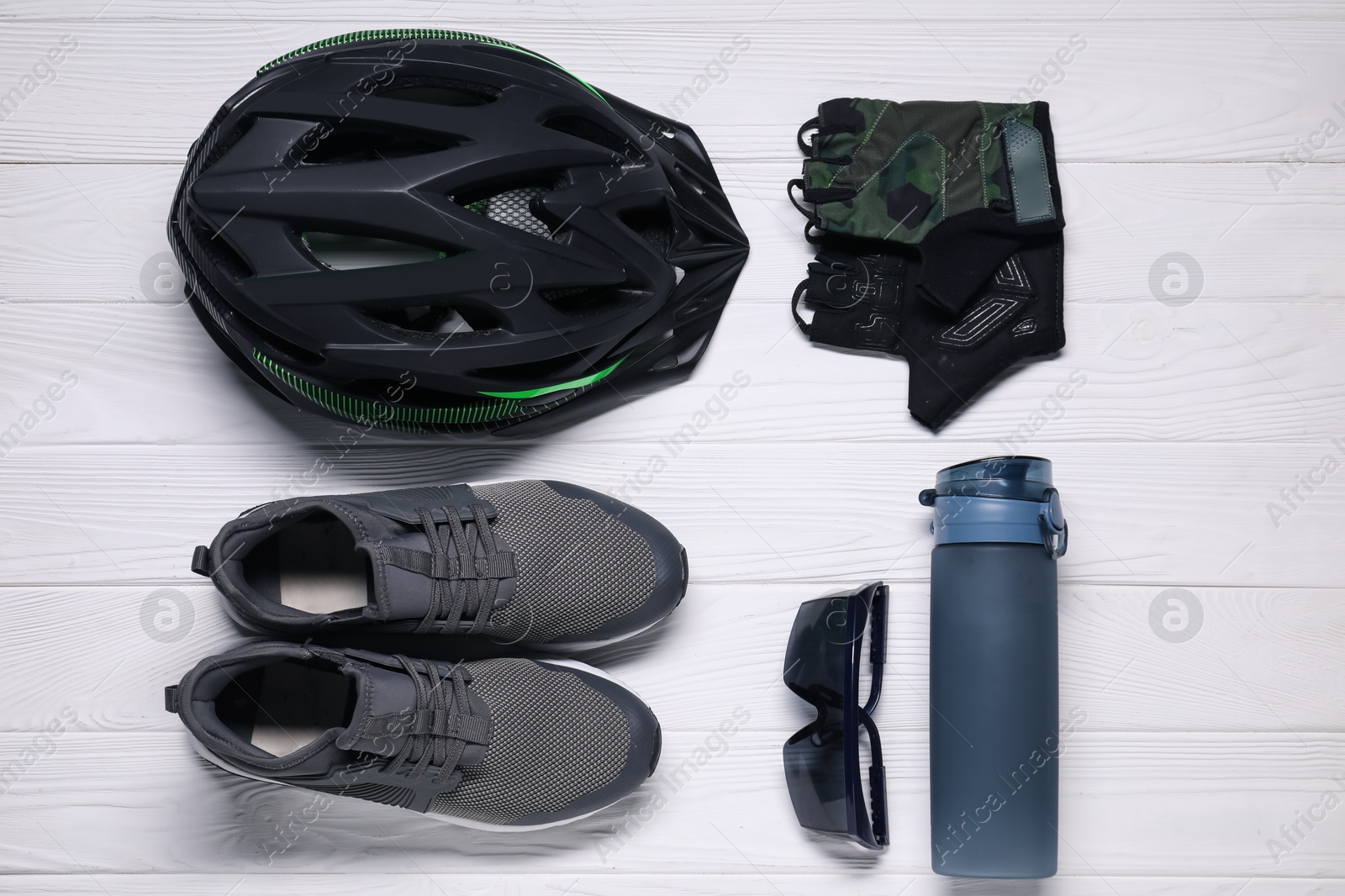 Photo of Bicycle helmet, sneakers, thermo bottle, fingerless gloves and goggles on white wooden background, flat lay