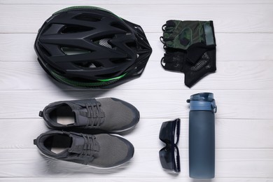 Bicycle helmet, sneakers, thermo bottle, fingerless gloves and goggles on white wooden background, flat lay