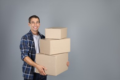 Moving into new house. Man with cardboard boxes on grey background, space for text