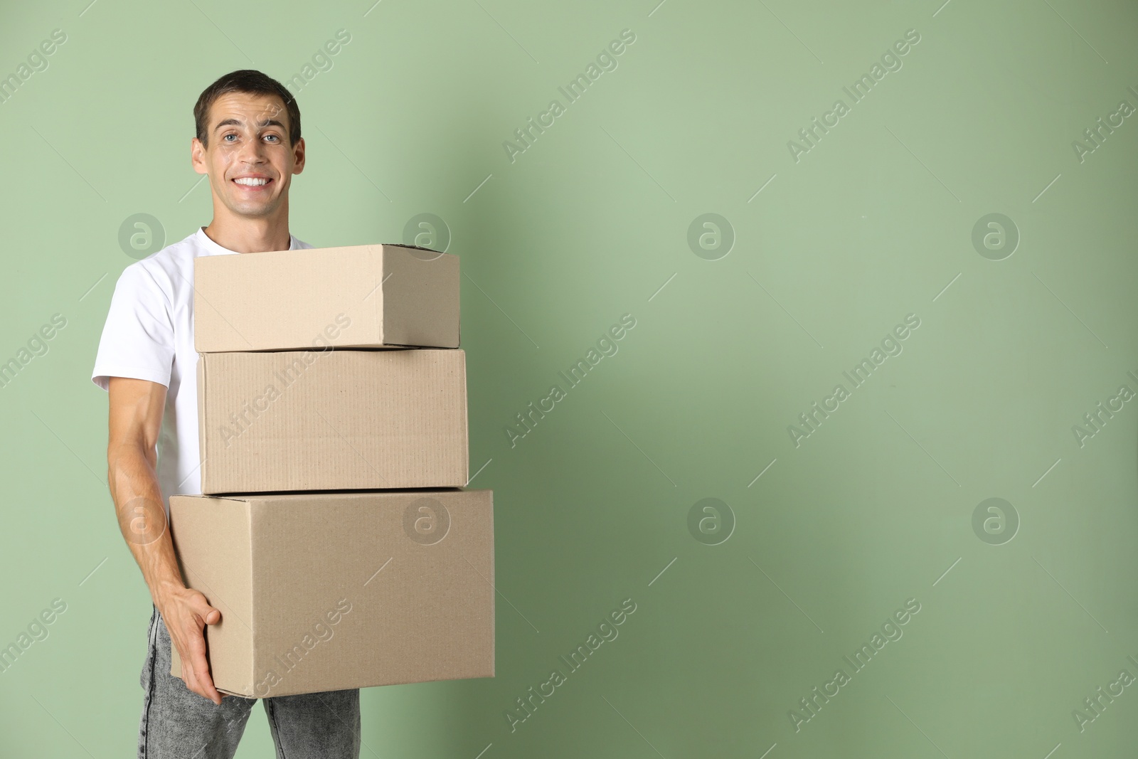 Photo of Moving into new house. Man with cardboard boxes on light green background, space for text