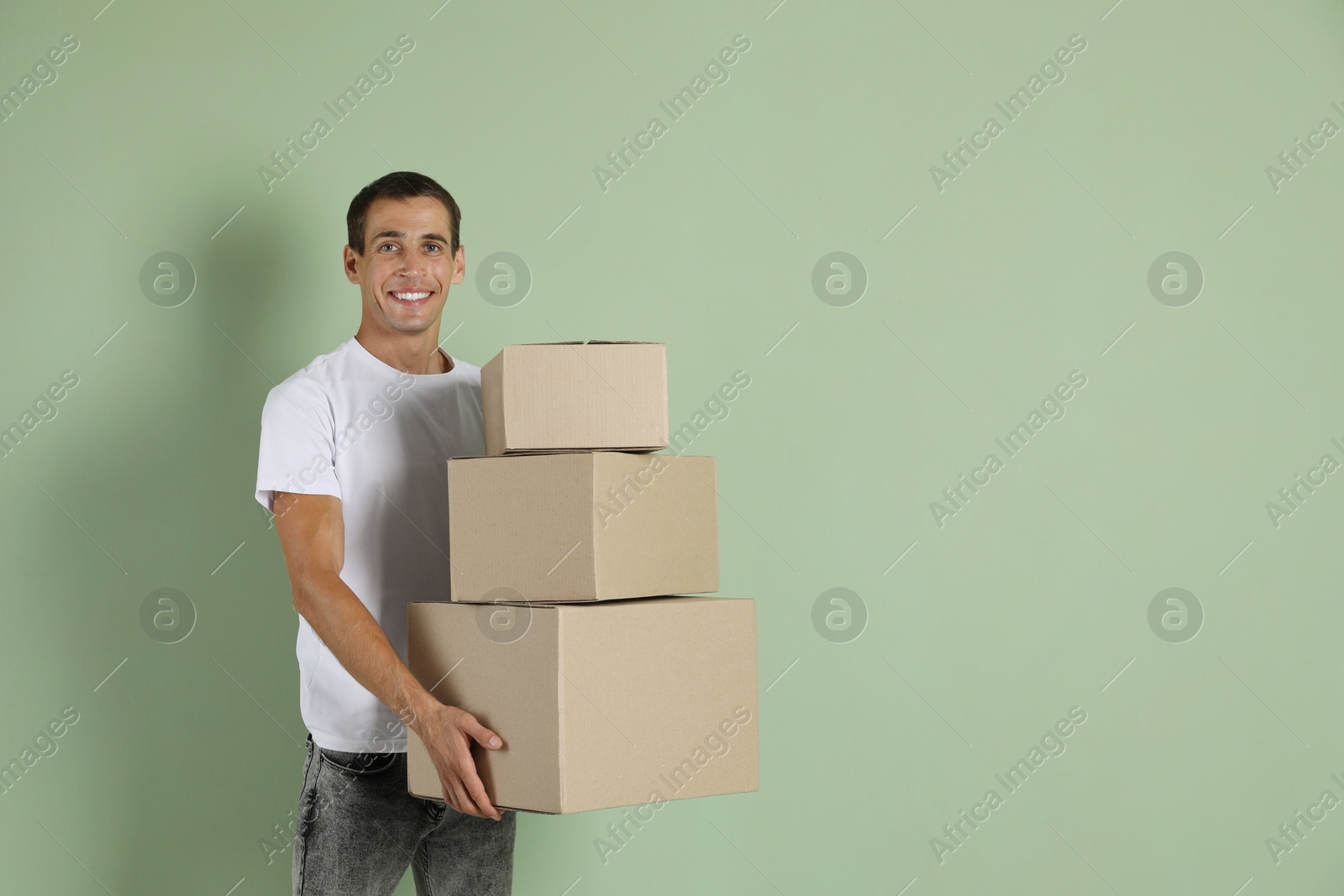 Photo of Moving into new house. Man with cardboard boxes on light green background, space for text