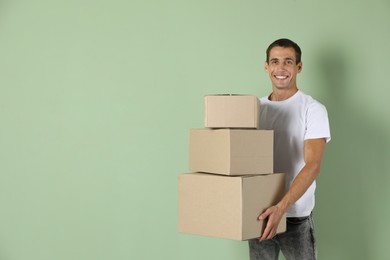 Photo of Moving into new house. Man with cardboard boxes on light green background, space for text