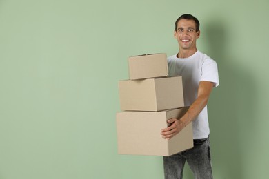 Photo of Moving into new house. Man with cardboard boxes on light green background, space for text