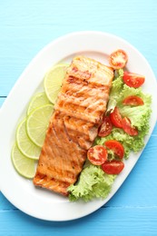 Photo of Delicious grilled salmon fillet with vegetable salad and lime on light blue wooden table, top view