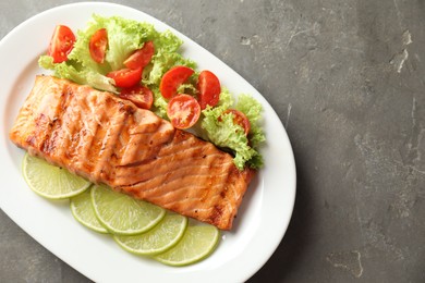 Delicious grilled salmon fillet with vegetable salad and lime on grey textured table, top view. Space for text