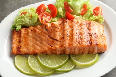 Photo of Delicious grilled salmon fillet with vegetable salad and lime on grey table, closeup