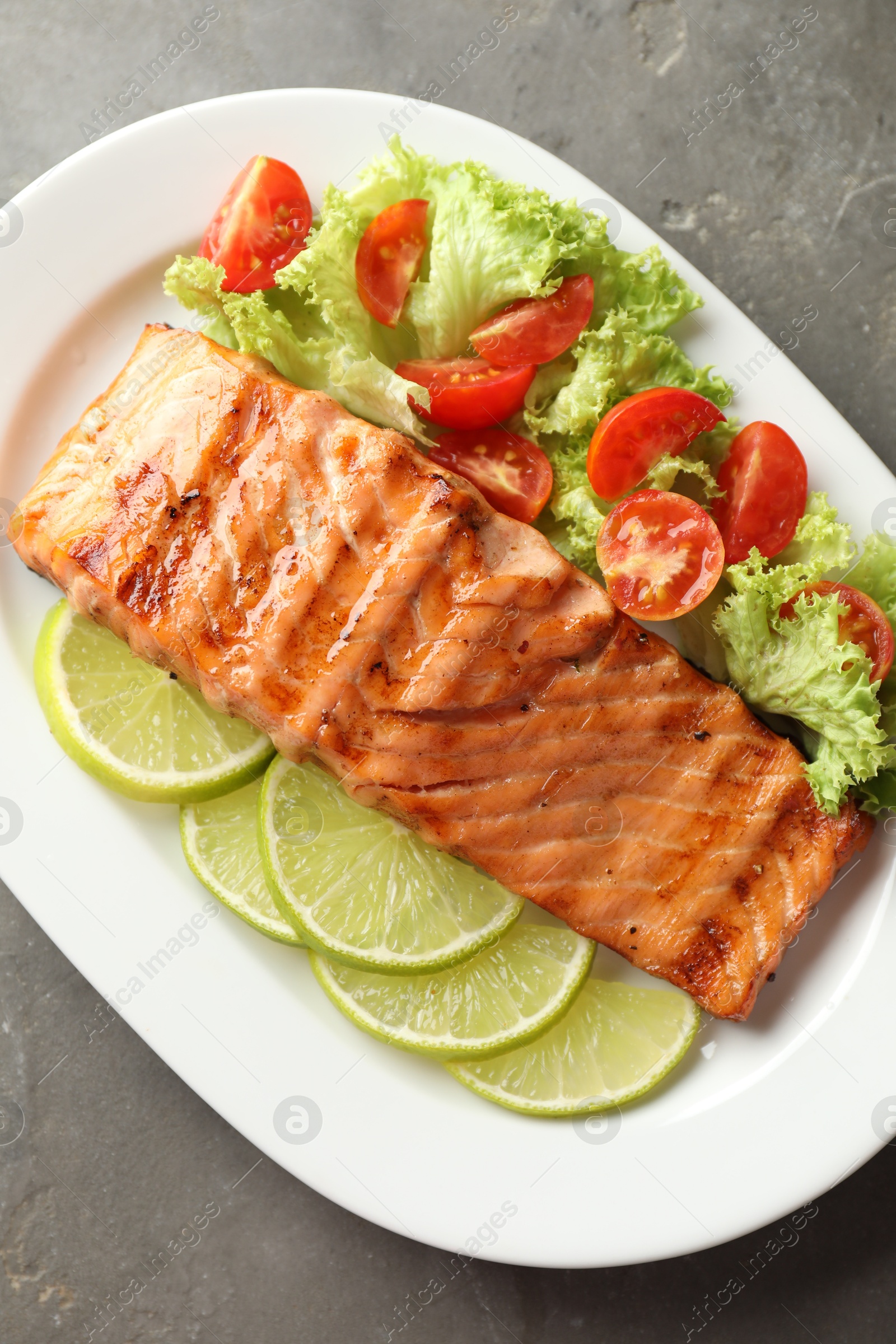 Photo of Delicious grilled salmon fillet with vegetable salad and lime on grey textured table, top view