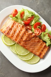 Delicious grilled salmon fillet with vegetable salad and lime on grey textured table, top view