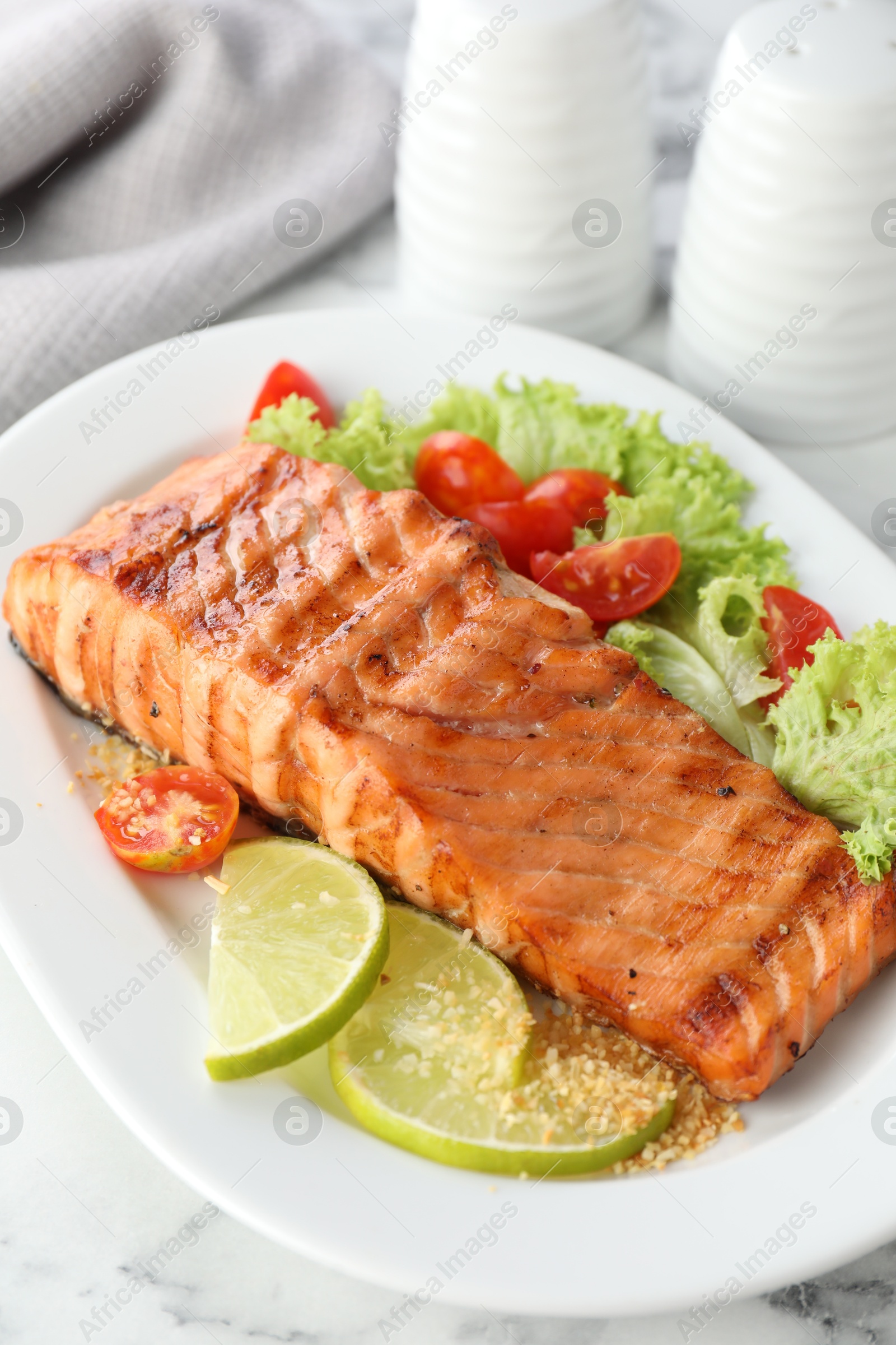 Photo of Delicious grilled salmon fillet with vegetable salad and lime on white marble table, closeup