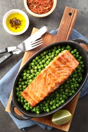 Photo of Delicious grilled salmon fillet in baking dish served on grey textured table, flat lay