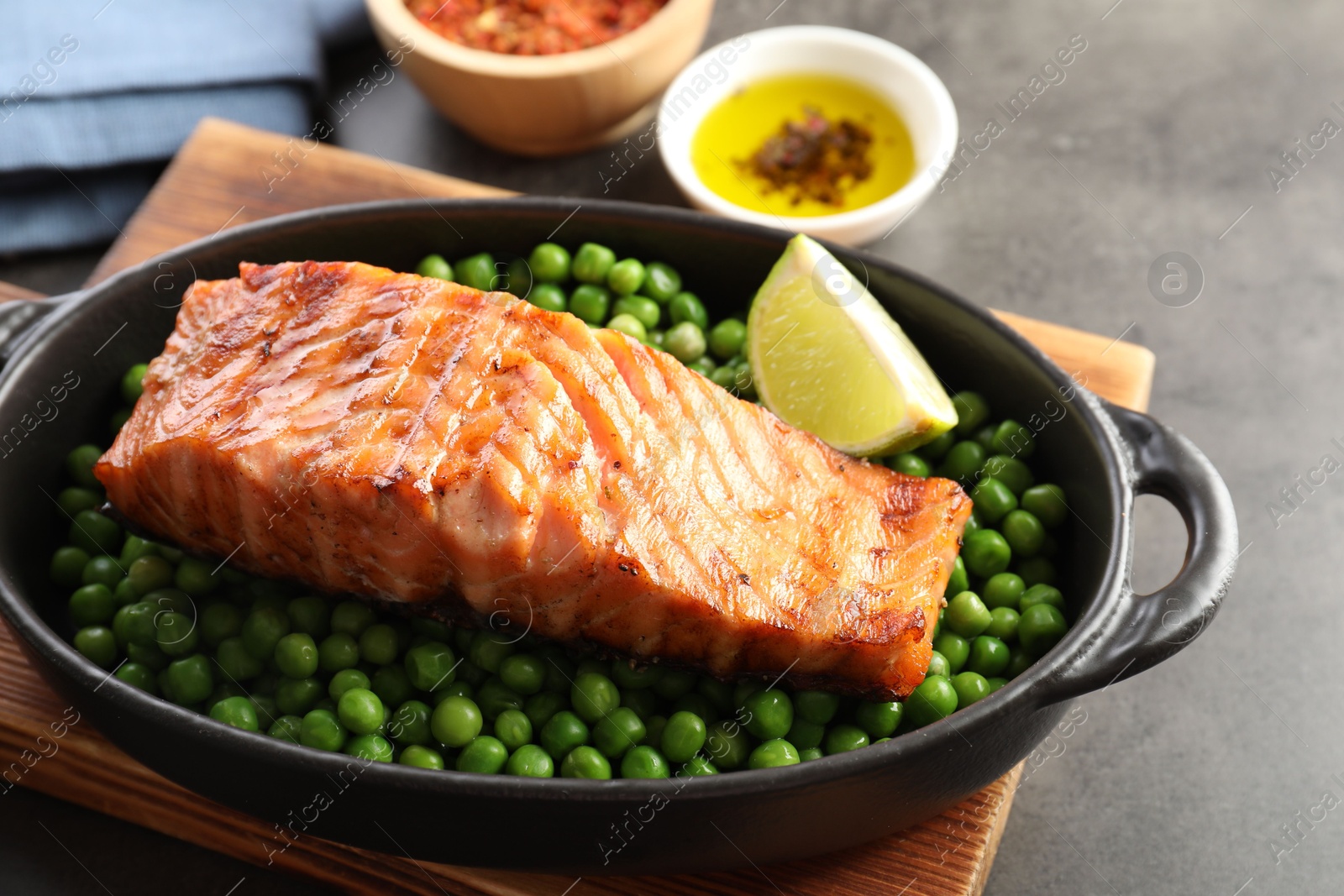 Photo of Delicious grilled salmon fillet with green peas and lime in baking dish on grey table, closeup