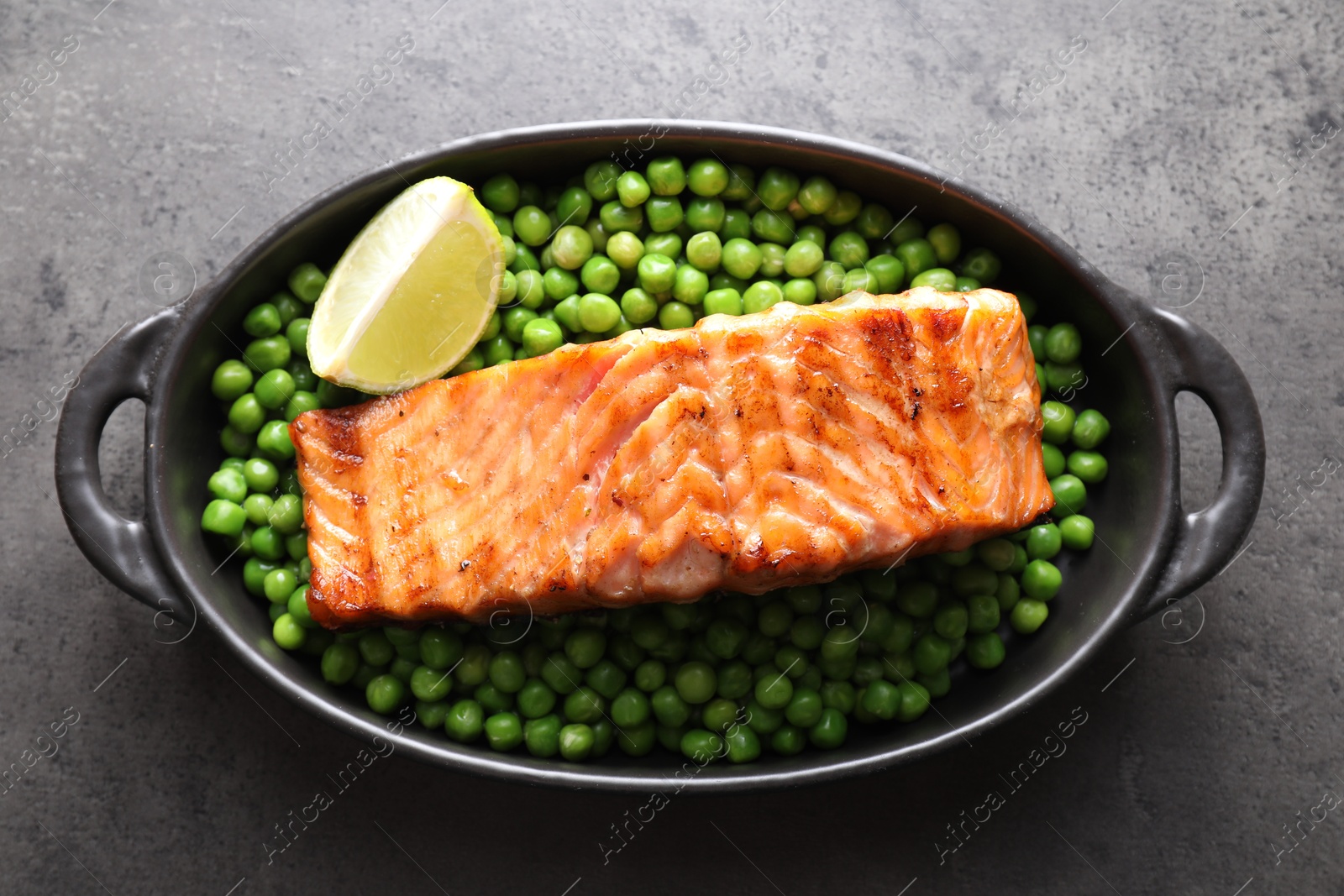 Photo of Delicious grilled salmon fillet with green peas and lime in baking dish on grey textured table, top view