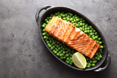 Photo of Delicious grilled salmon fillet with green peas and lime in baking dish on grey textured table, top view