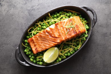 Photo of Delicious grilled salmon fillet with green peas and lime in baking dish on grey textured table, top view