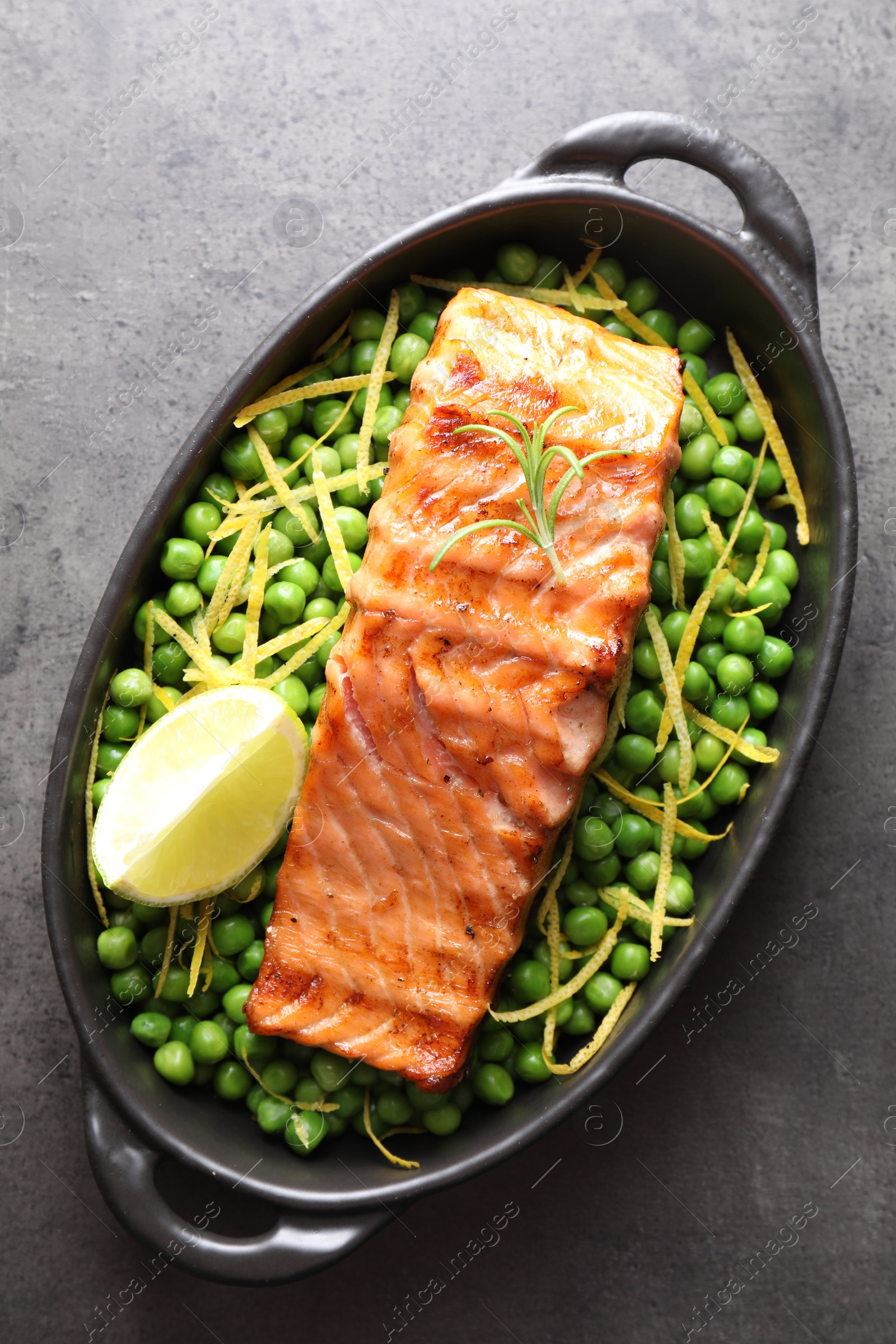 Photo of Delicious grilled salmon fillet with green peas and lime in baking dish on grey textured table, top view