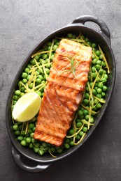 Photo of Delicious grilled salmon fillet with green peas and lime in baking dish on grey textured table, top view