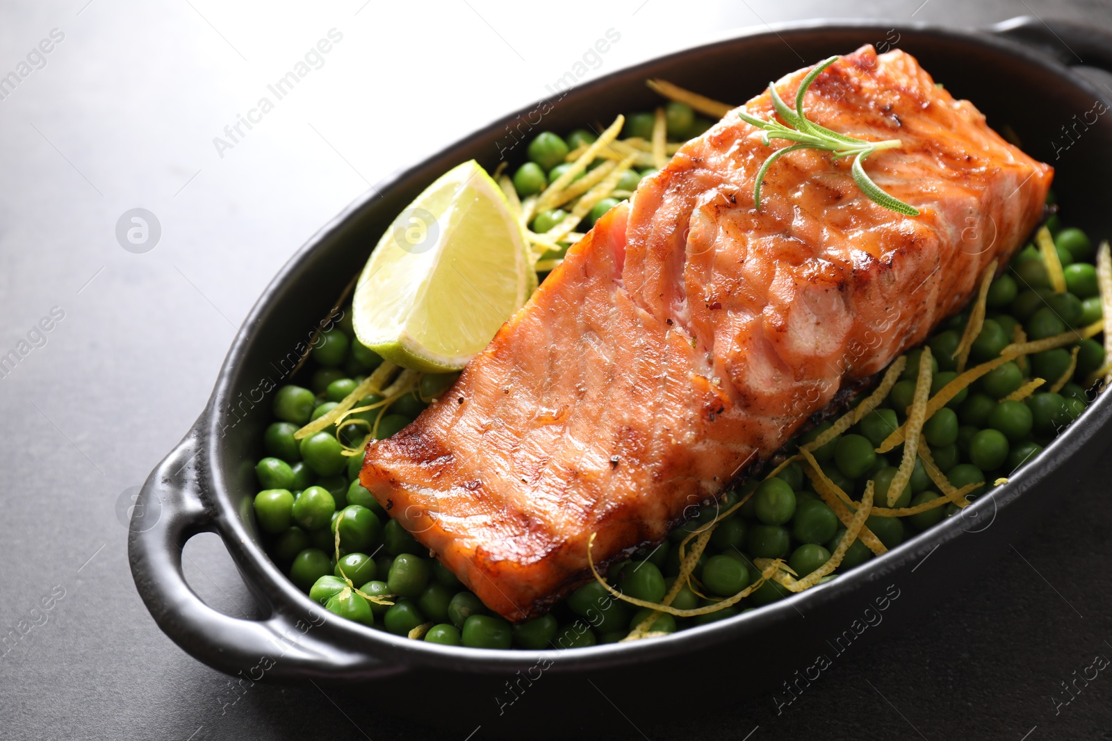 Photo of Delicious grilled salmon fillet with green peas and lime in baking dish on grey table, closeup