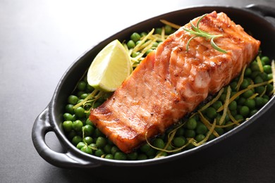 Photo of Delicious grilled salmon fillet with green peas and lime in baking dish on grey table, closeup